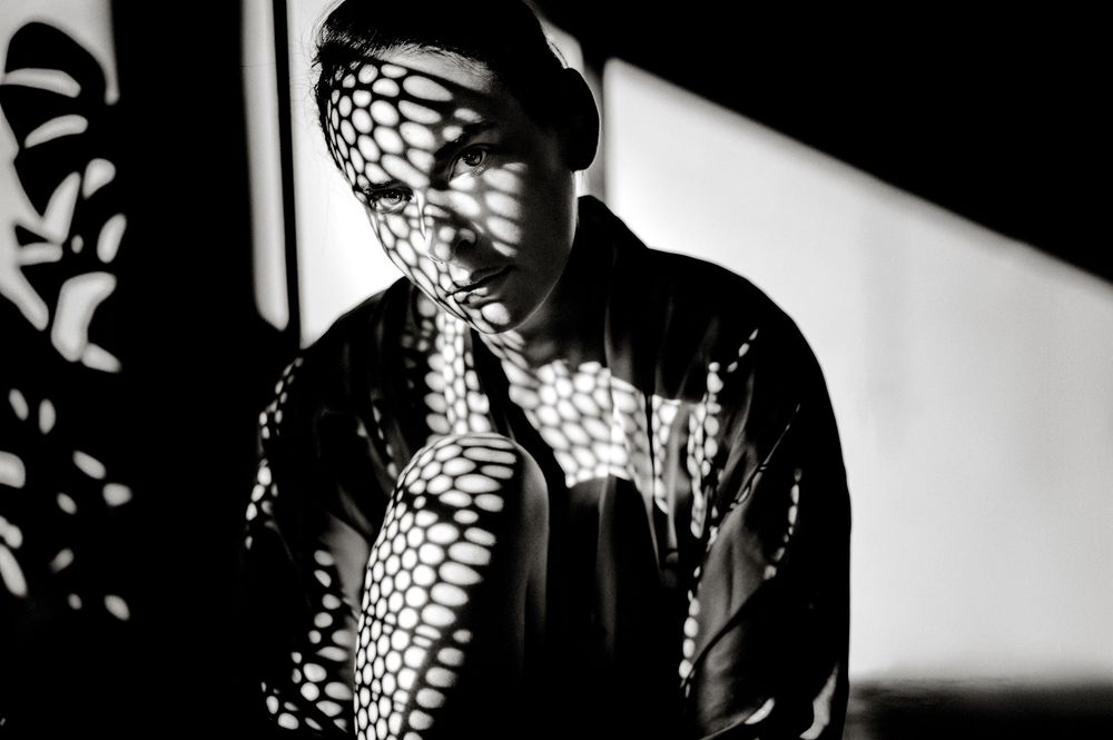 Black and white portrait of a person with dramatic net shadow pattern across face and jacket.