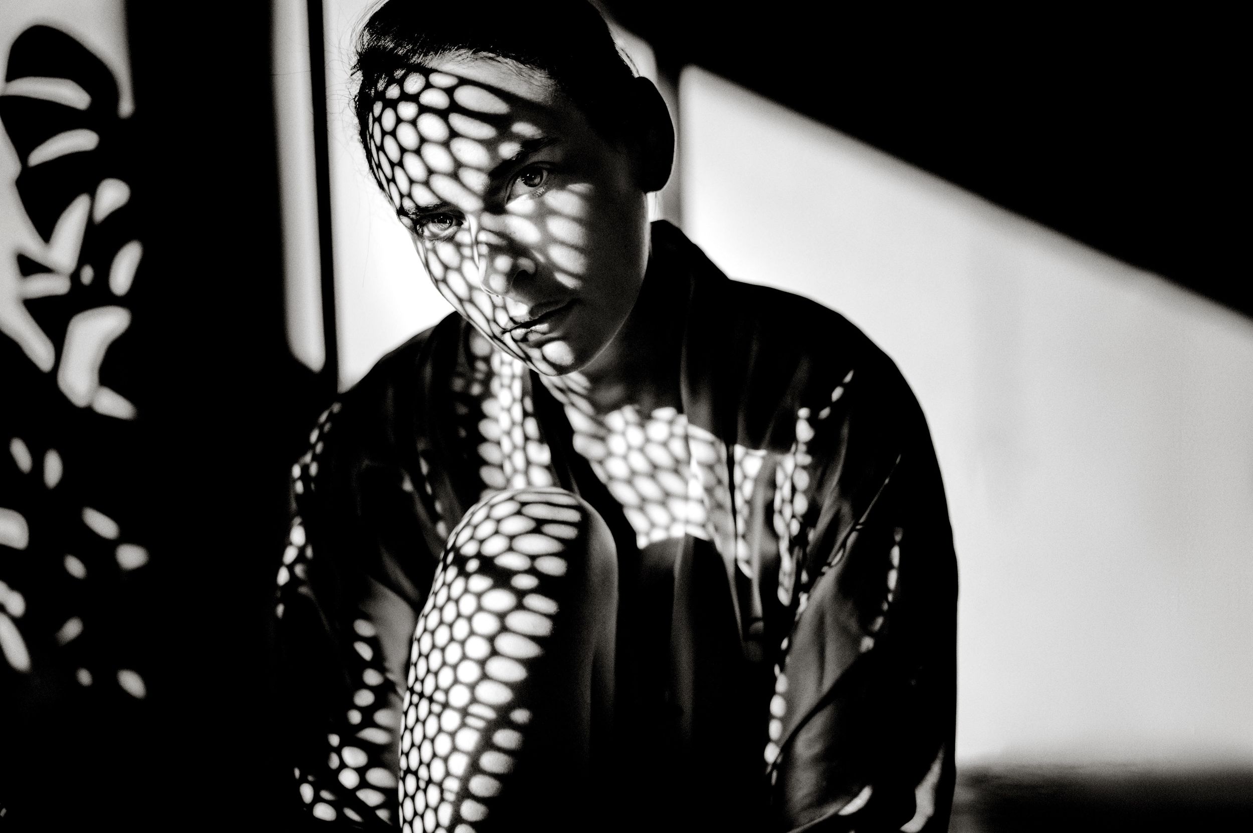 Black and white portrait of a person with dramatic net shadow pattern across face and jacket.