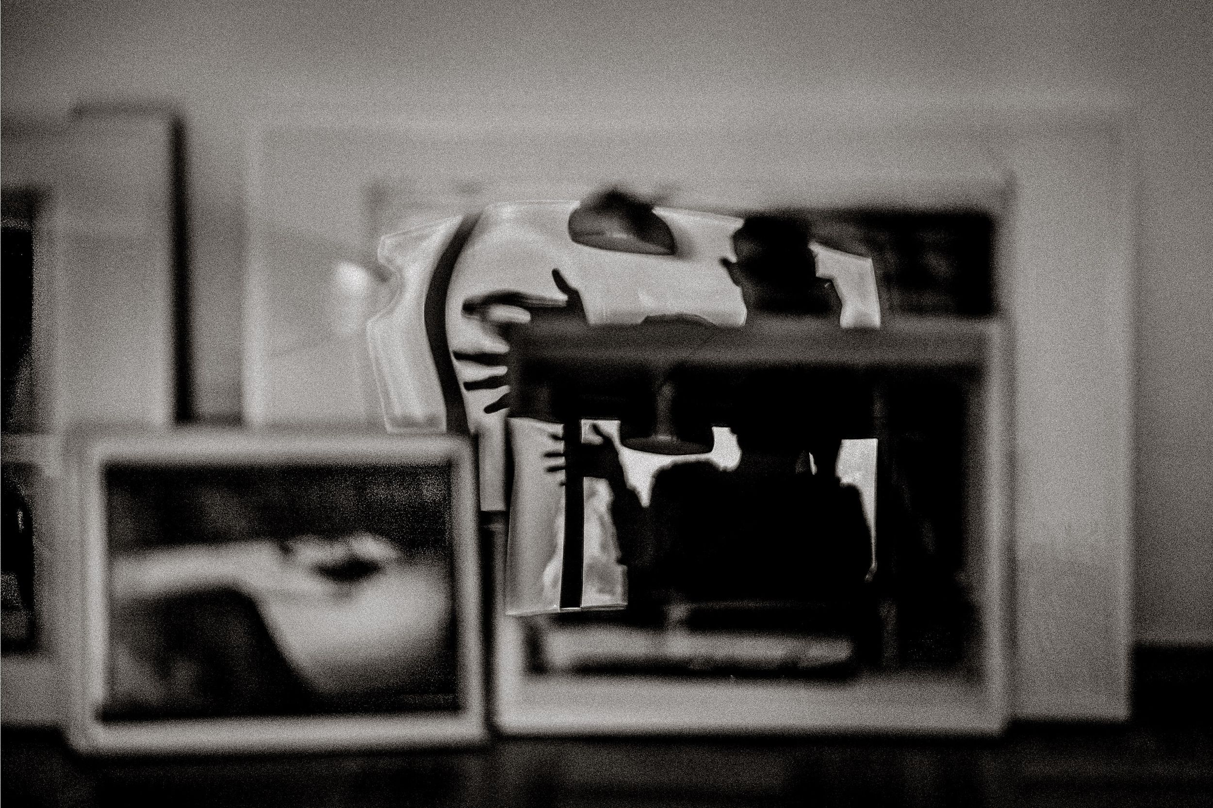 Black and white photo of framed pictures displayed on a surface, with reflections creating an artistic layered effect.
