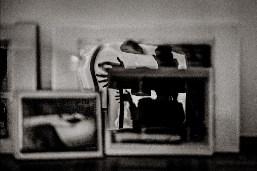 Black and white photo of framed pictures displayed on a surface, with reflections creating an artistic layered effect.