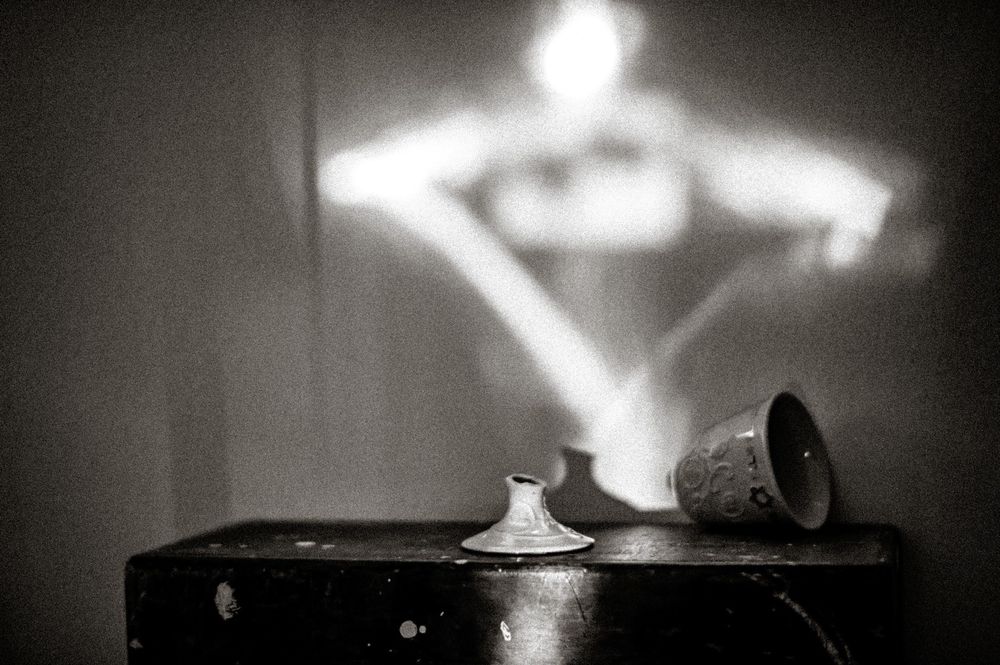 Black and white photo of ceramic vessels on a dark wooden surface with dramatic light projection on wall.