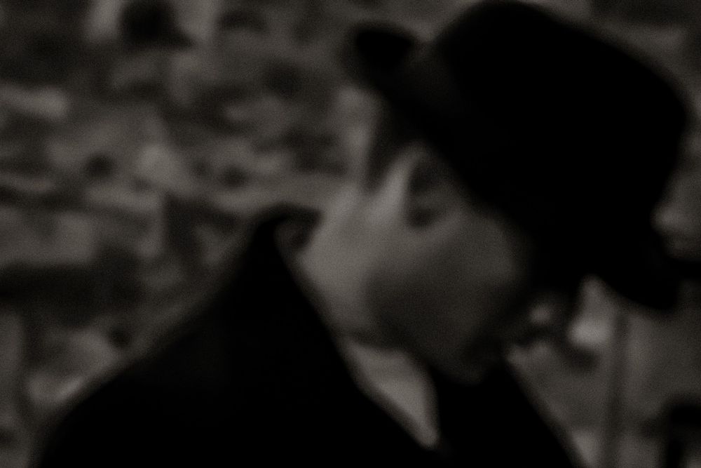 Black and white blurred portrait of a man wearing a bowler hat outdoors.