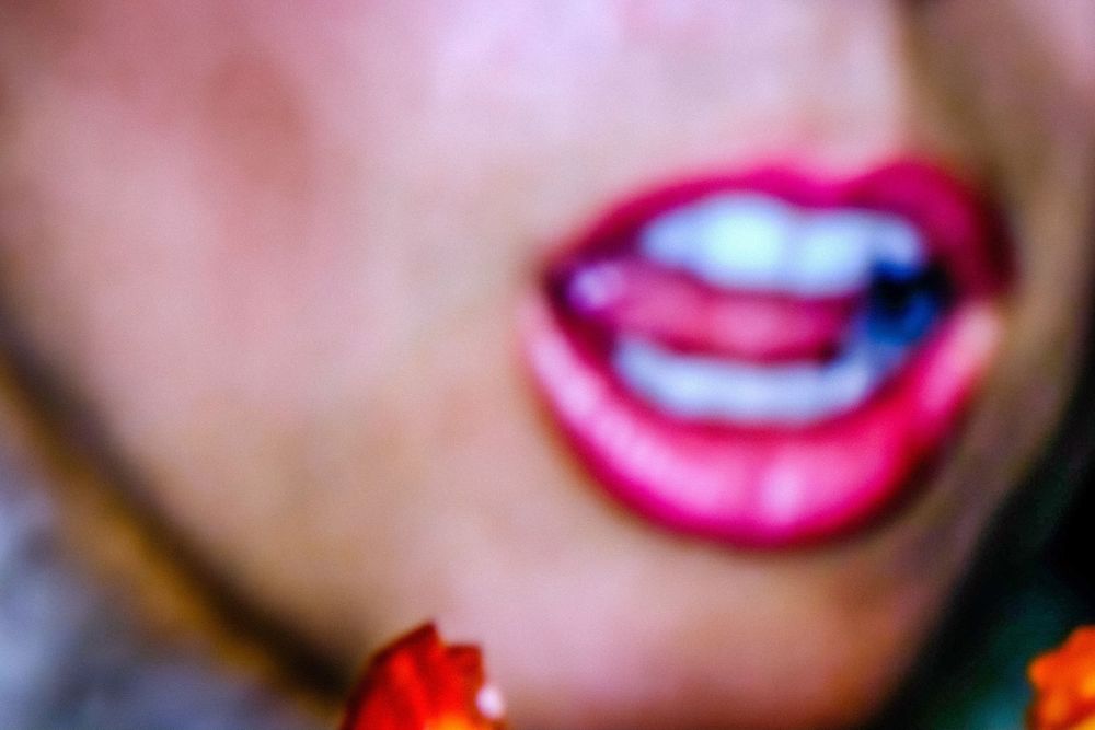 Close-up of bold red lipstick on slightly open lips showing white teeth, with red floral accents below.