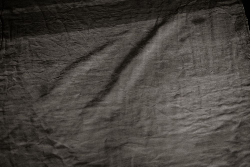Dark gray crumpled fabric texture with natural wrinkles and soft shadows creating depth.