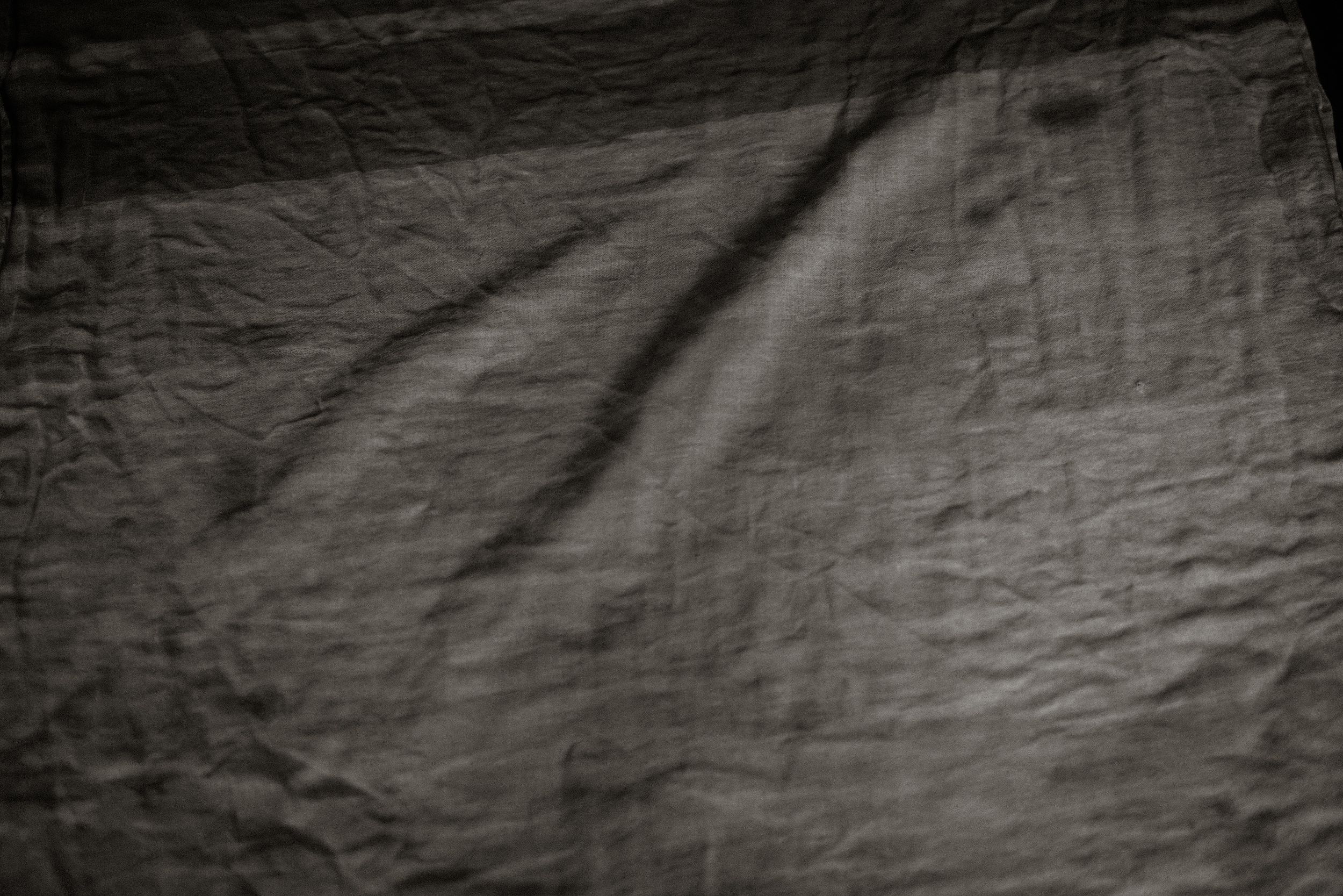 Dark gray crumpled fabric texture with natural wrinkles and soft shadows creating depth.