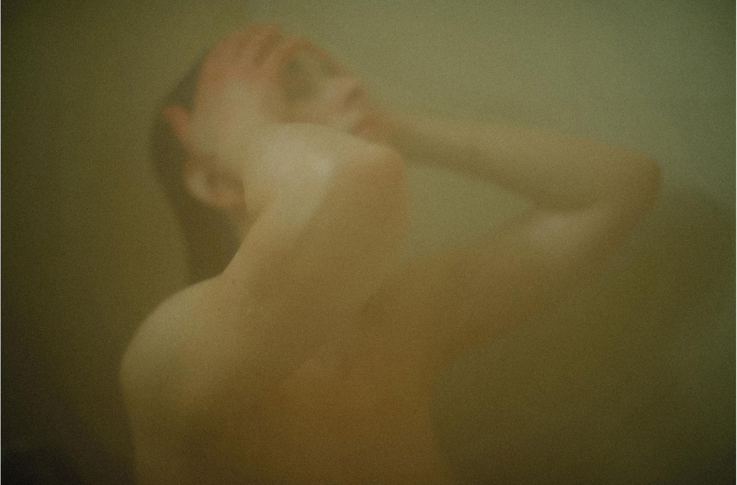 A hazy, atmospheric photo of a person in a steamy shower, captured in warm, muted tones.