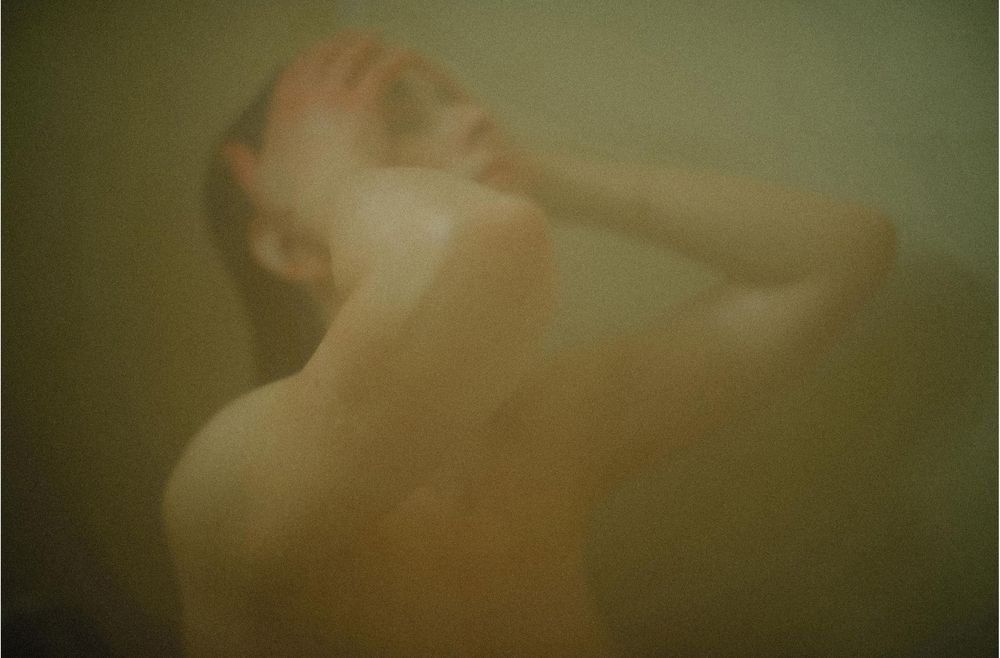 A hazy, atmospheric photo of a person in a steamy shower, captured in warm, muted tones.