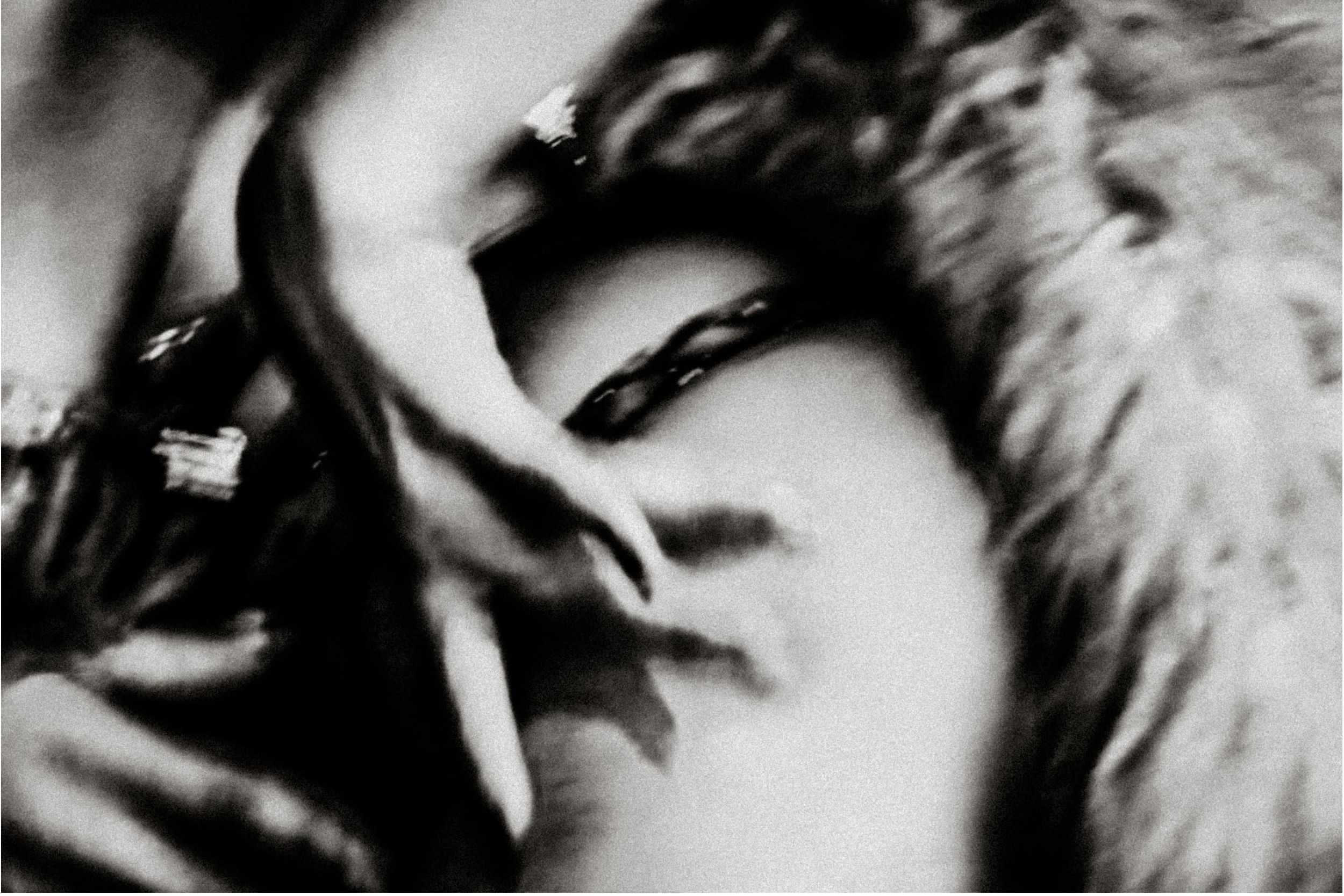 Black and white close-up photo of a woman with dramatic shadows, wearing fur, hand near face.