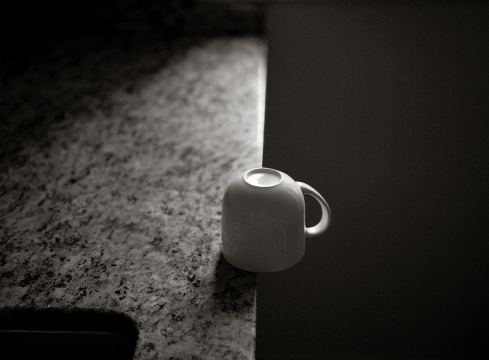 White ceramic mug sitting on edge of granite countertop in dramatic black and white lighting.