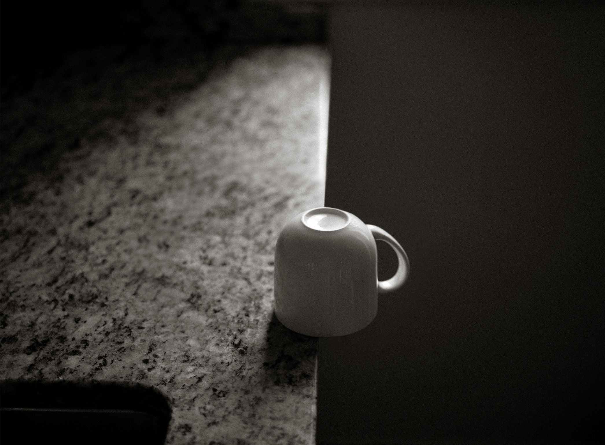 White ceramic mug sitting on edge of granite countertop in dramatic black and white lighting.
