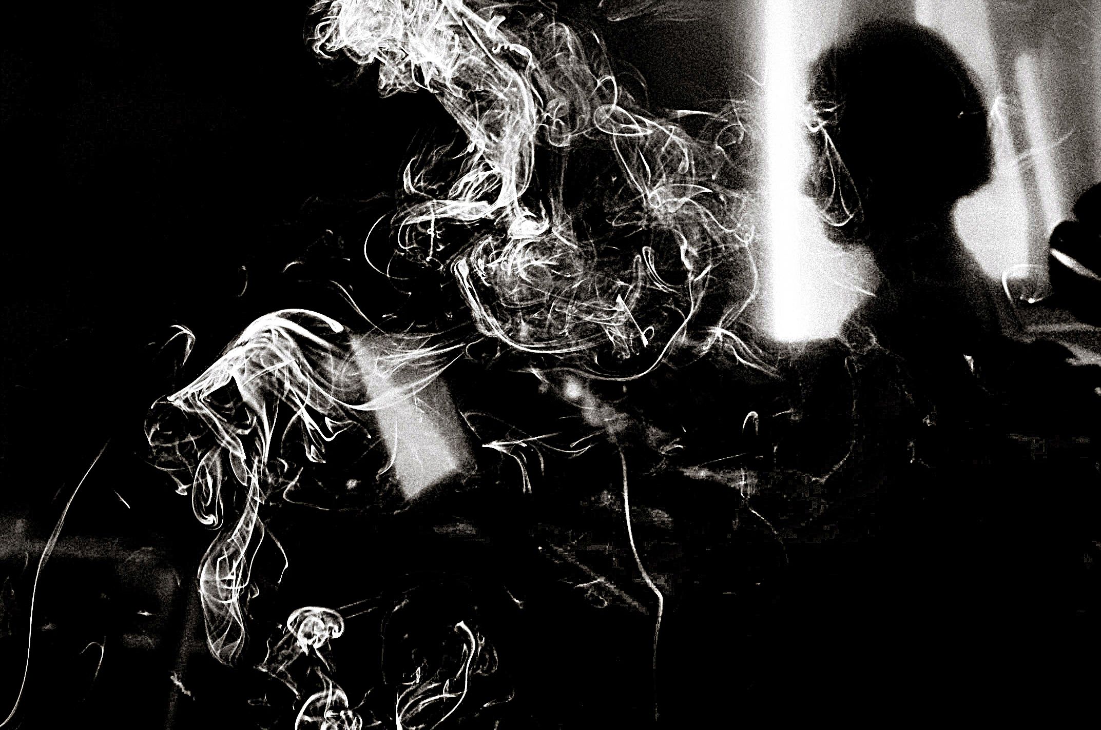 Black and white photo of a silhouetted figure surrounded by swirling smoke in dramatic contrast lighting.