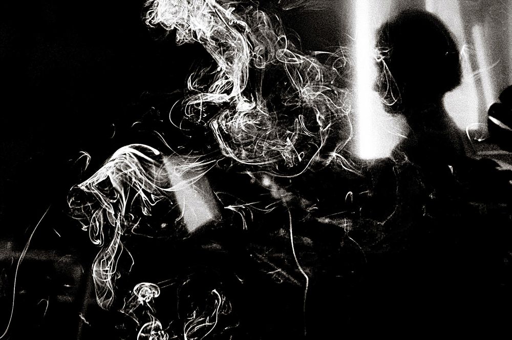 Black and white photo of a silhouetted figure surrounded by swirling smoke in dramatic contrast lighting.