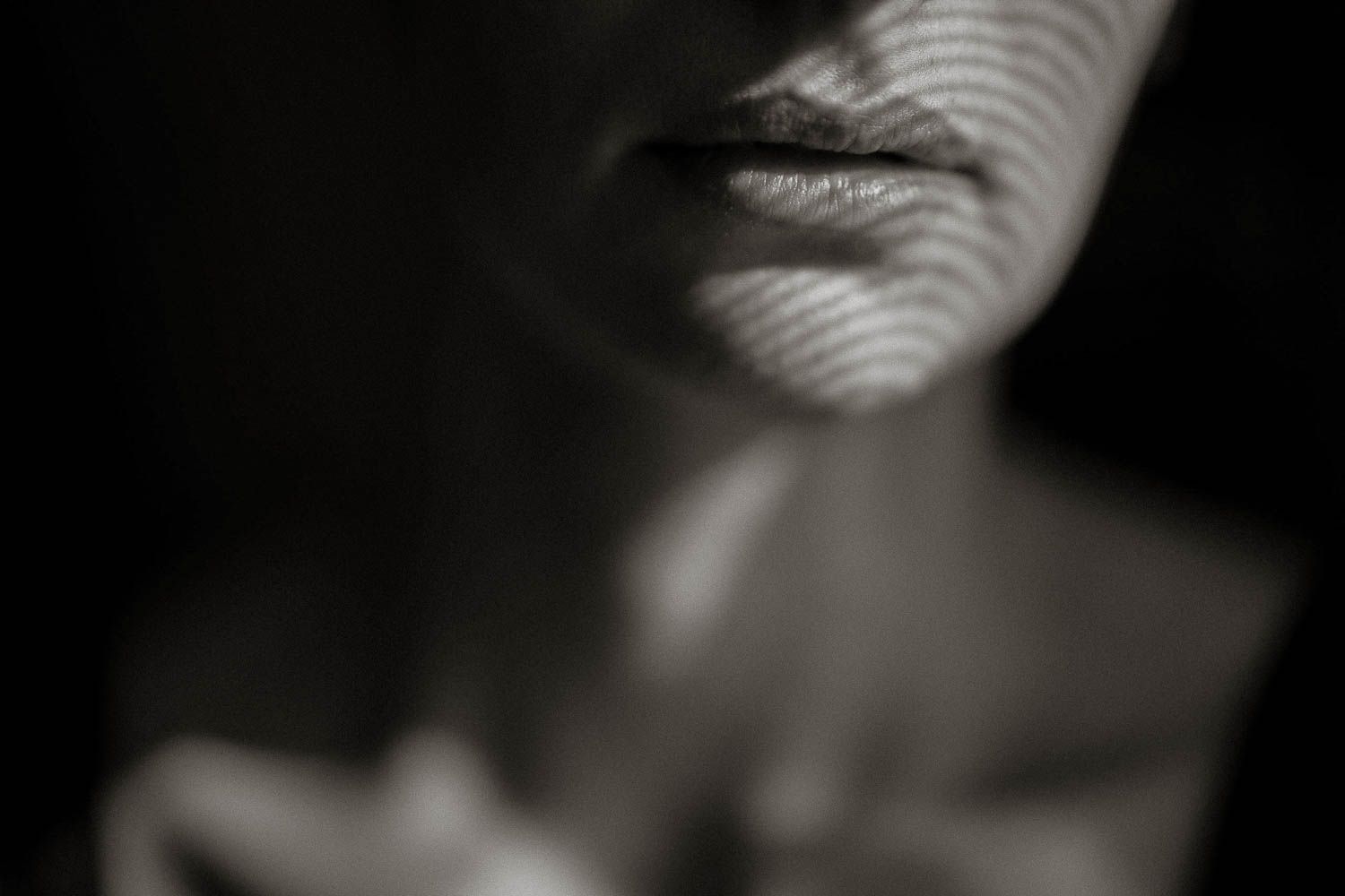 Black and white close-up portrait with dramatic striped shadow patterns across a woman's lips and neck.