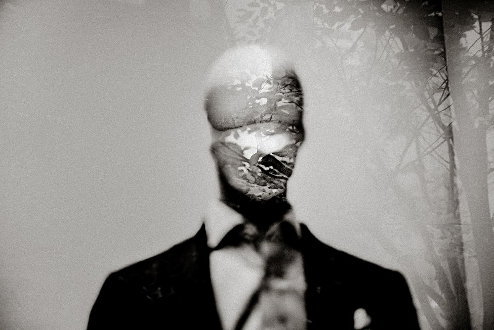 Eerie black and white double exposure portrait of a faceless man in a suit and tie with forest overlay.