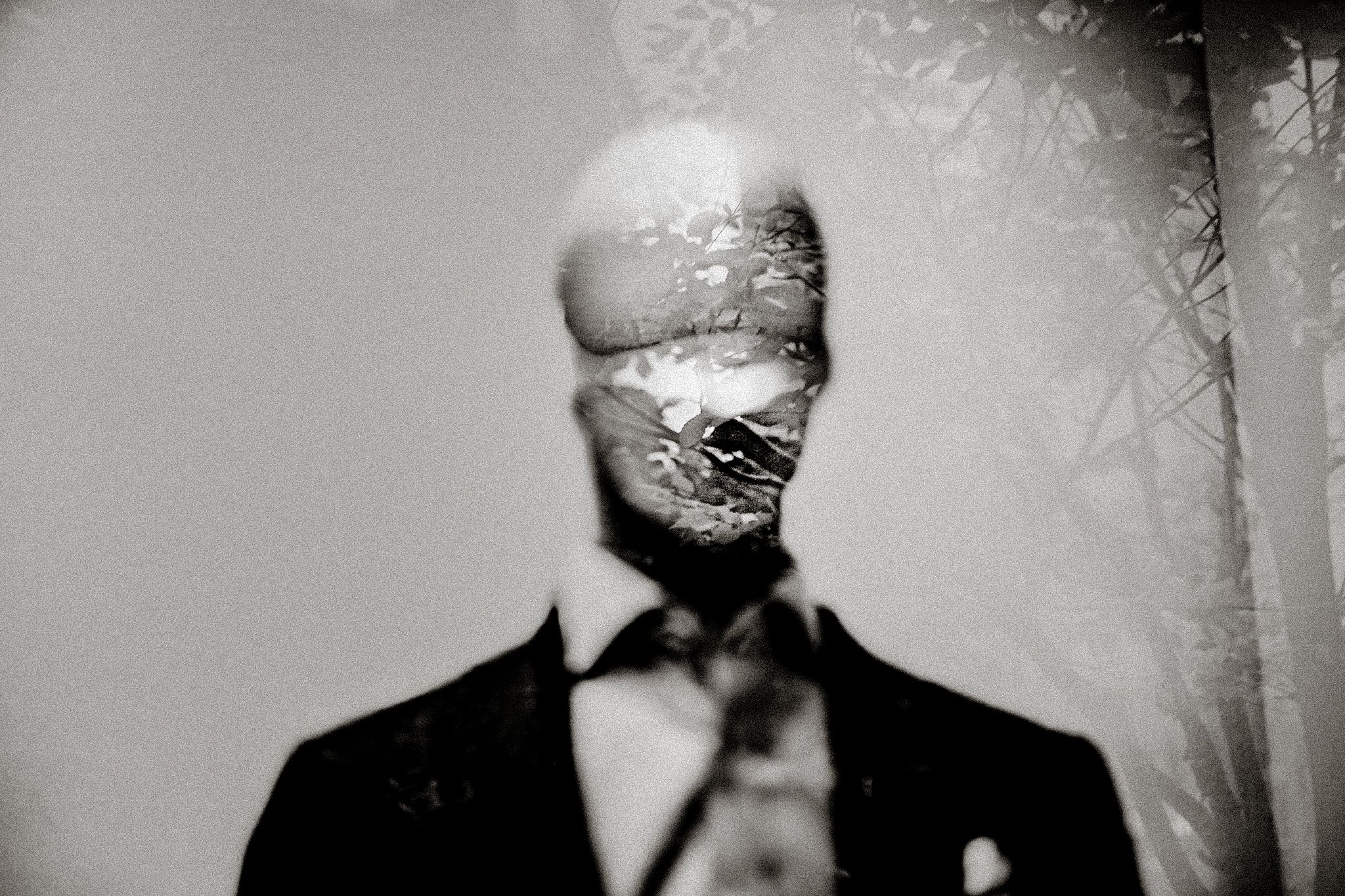 Eerie black and white double exposure portrait of a faceless man in a suit and tie with forest overlay.