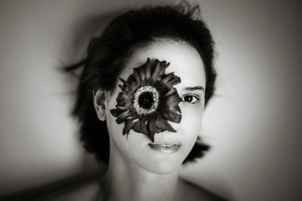 Black and white portrait of a woman with a large flower covering one eye, creating a surreal artistic effect.