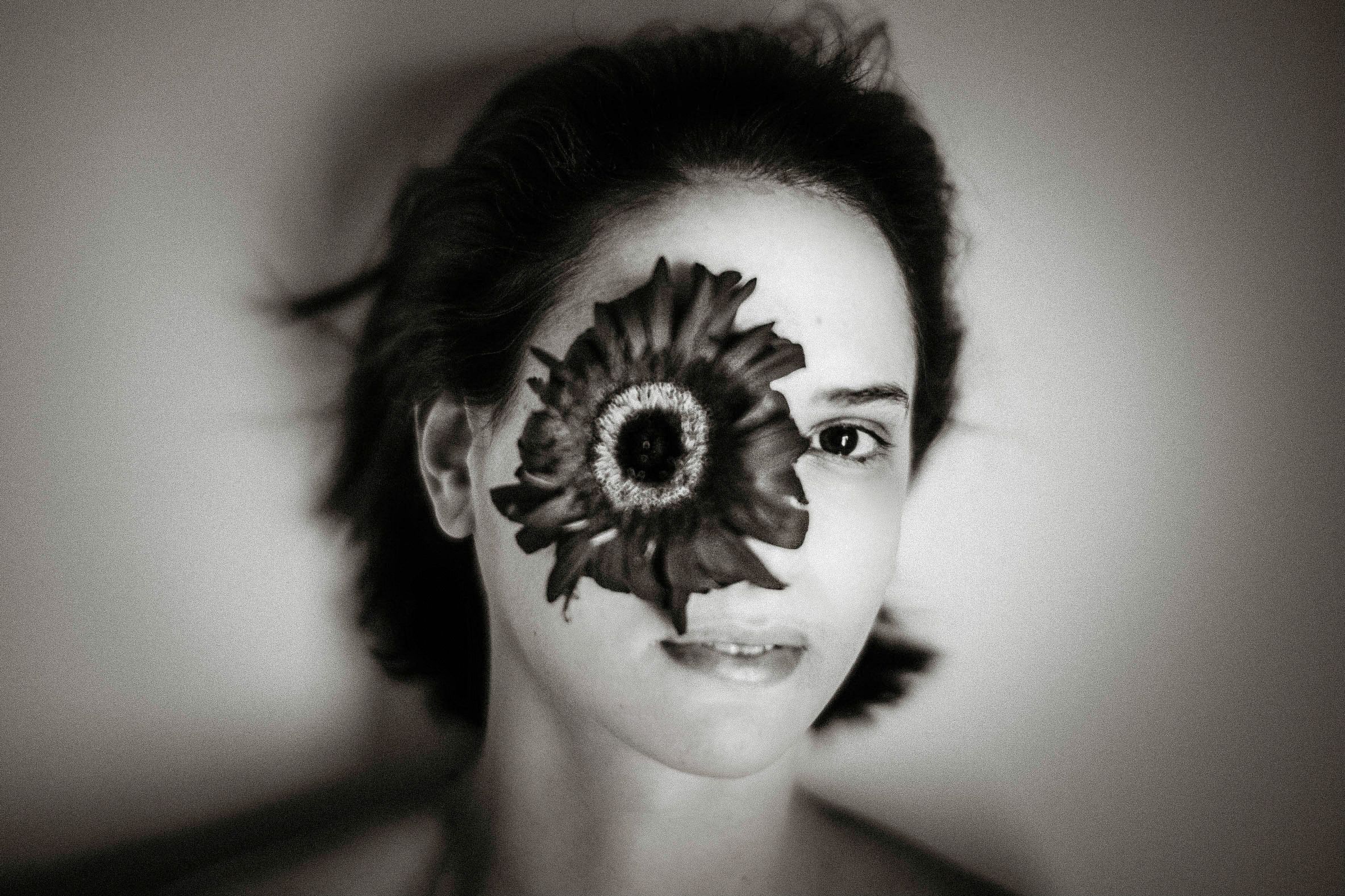 Black and white portrait of a woman with a large flower covering one eye, creating a surreal artistic effect.
