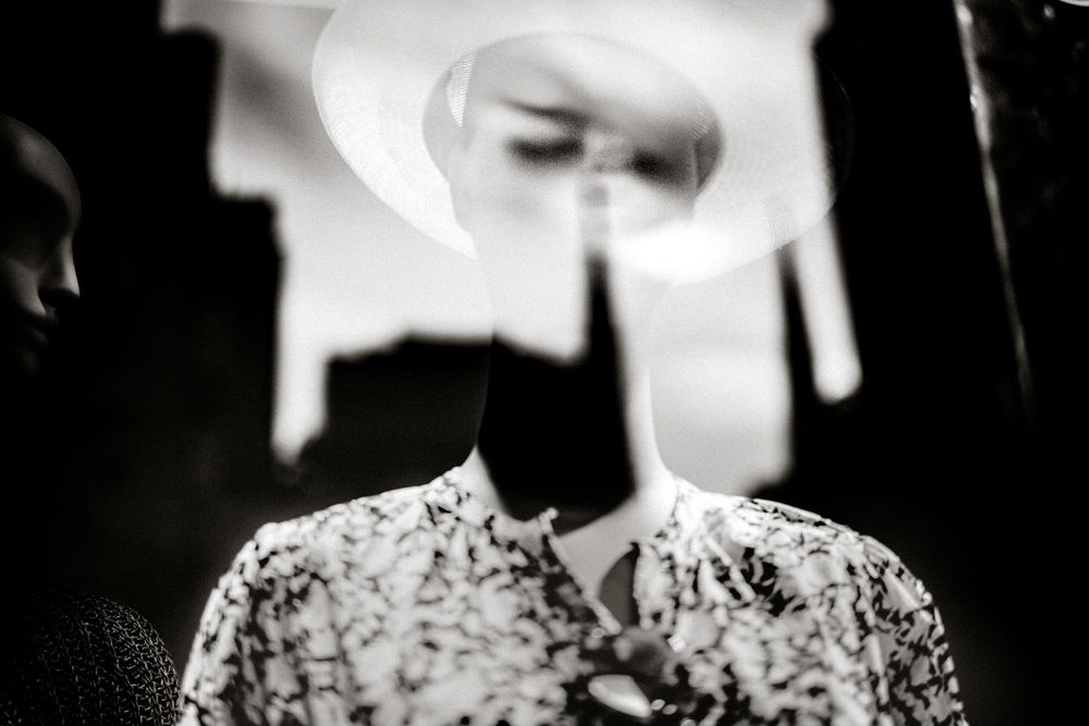 Black and white double exposure portrait of a person in floral shirt wearing a wide-brim hat, artistic surreal photography.