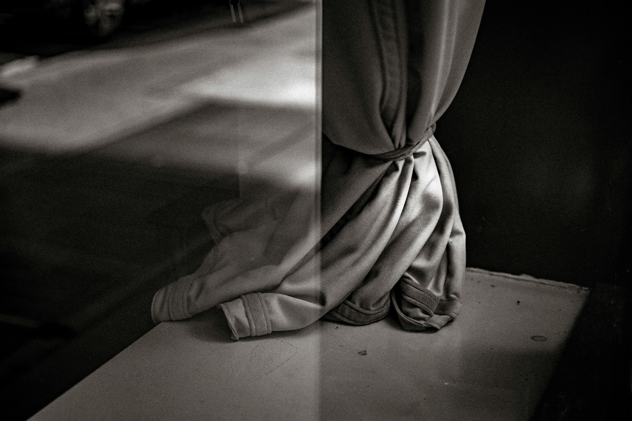 Black and white photo of draped fabric tied at the base of a column on a ledge.