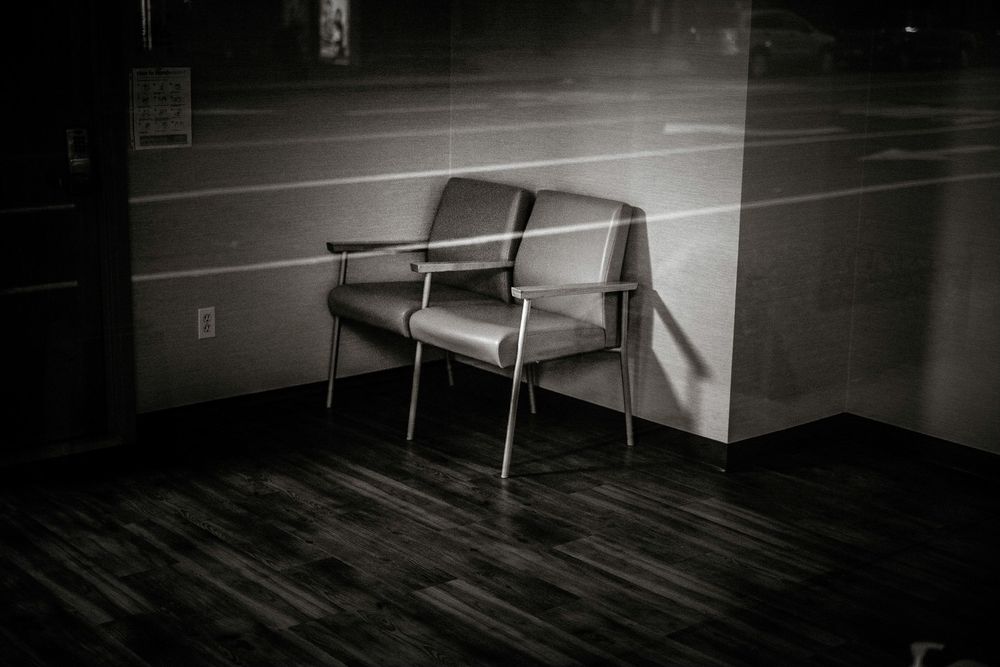 A lone vintage chair sits in a dimly lit room with dark hardwood floors in a moody black and white photo.