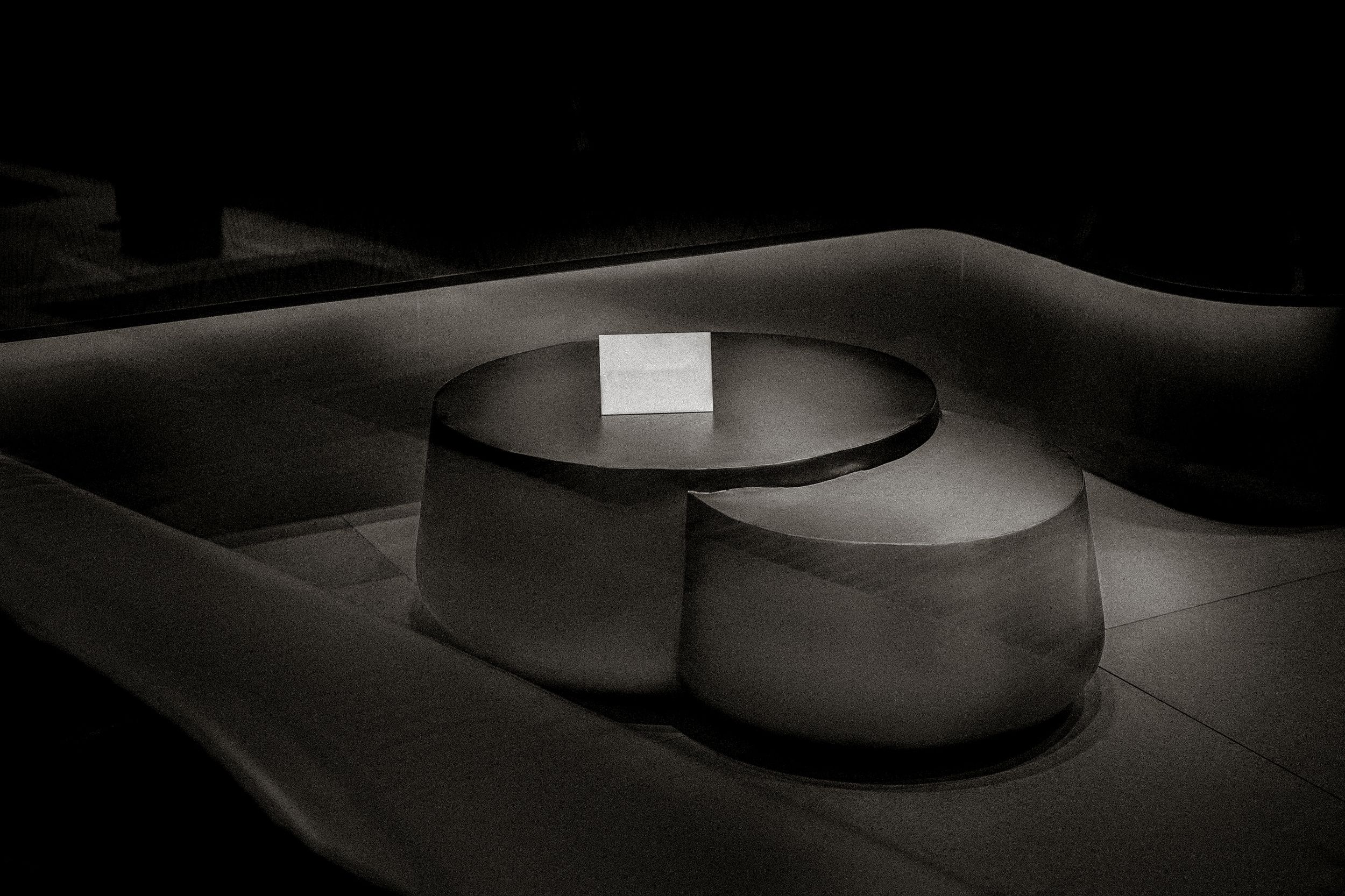 Modern round concrete coffee table set in a dimly lit lounge with curved white bench seating.