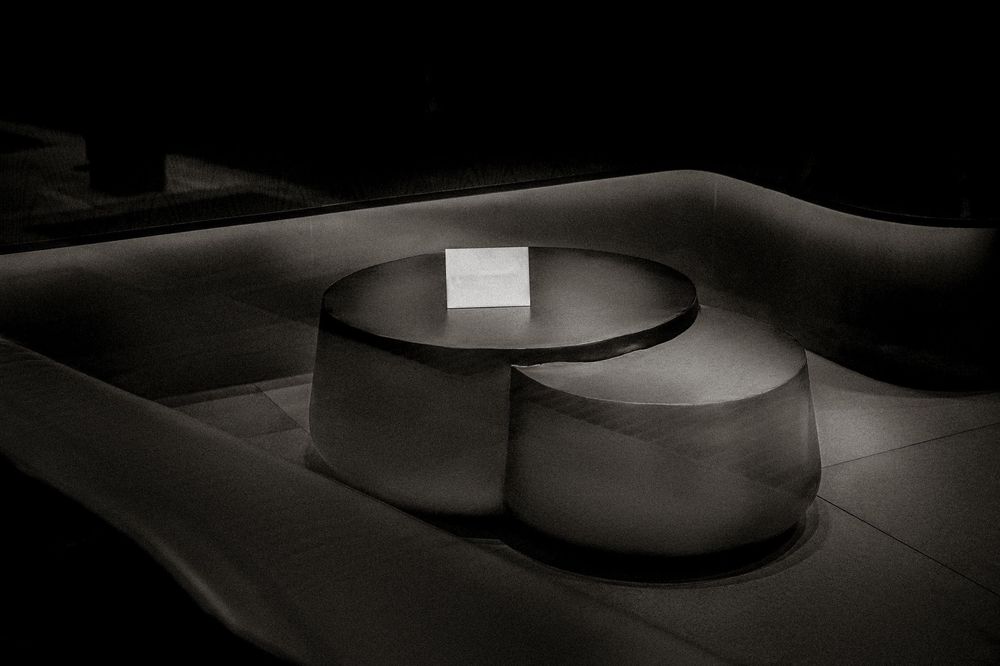 Modern round concrete coffee table set in a dimly lit lounge with curved white bench seating.