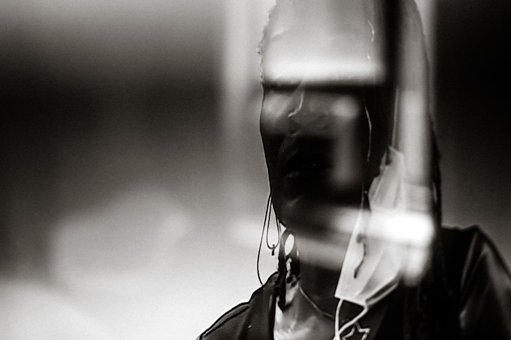 Black and white portrait of a hooded figure with earphones, shrouded in mysterious shadows and light.
