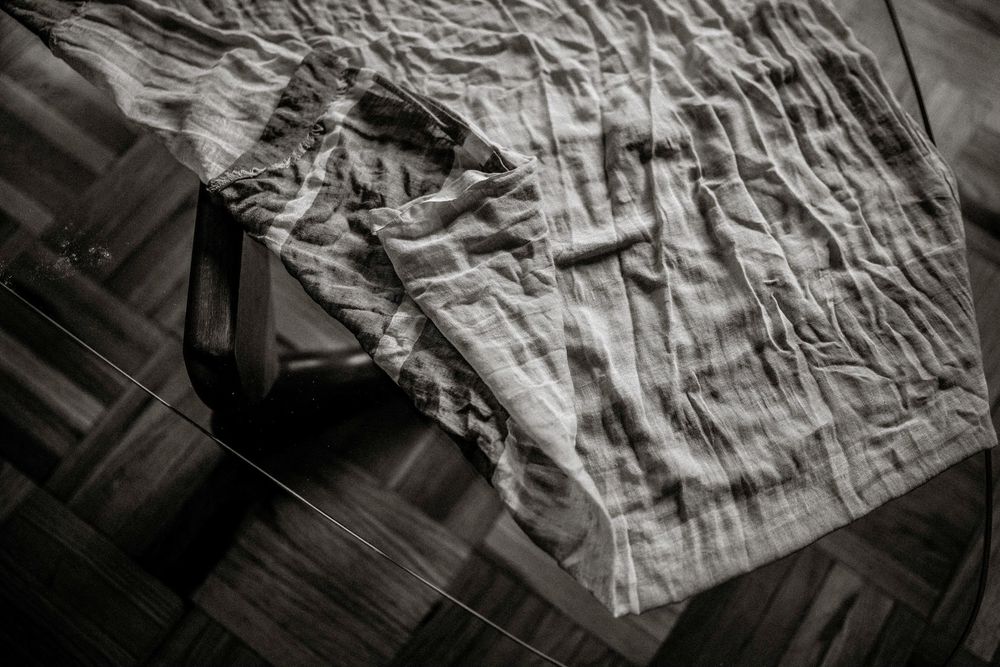 Black and white photo of a crumpled white sheet draped over a wooden floor.