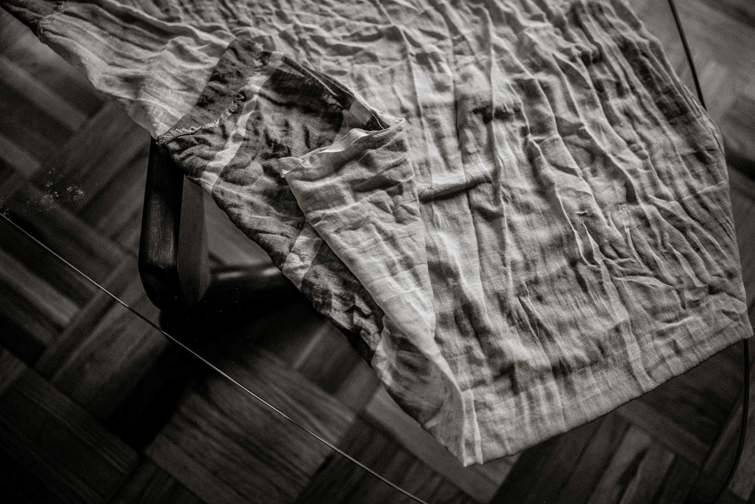 Black and white photo of a crumpled white sheet draped over a wooden floor.