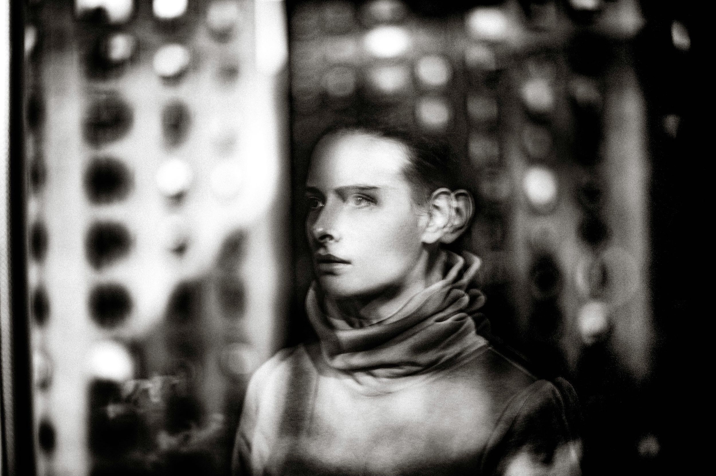 Black and white portrait of a young person wearing a turtleneck, gazing thoughtfully in dramatic studio lighting.
