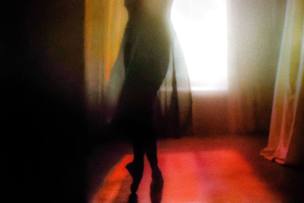 Silhouette of a person standing in a dimly lit room with dramatic red floor and glowing curtained window.