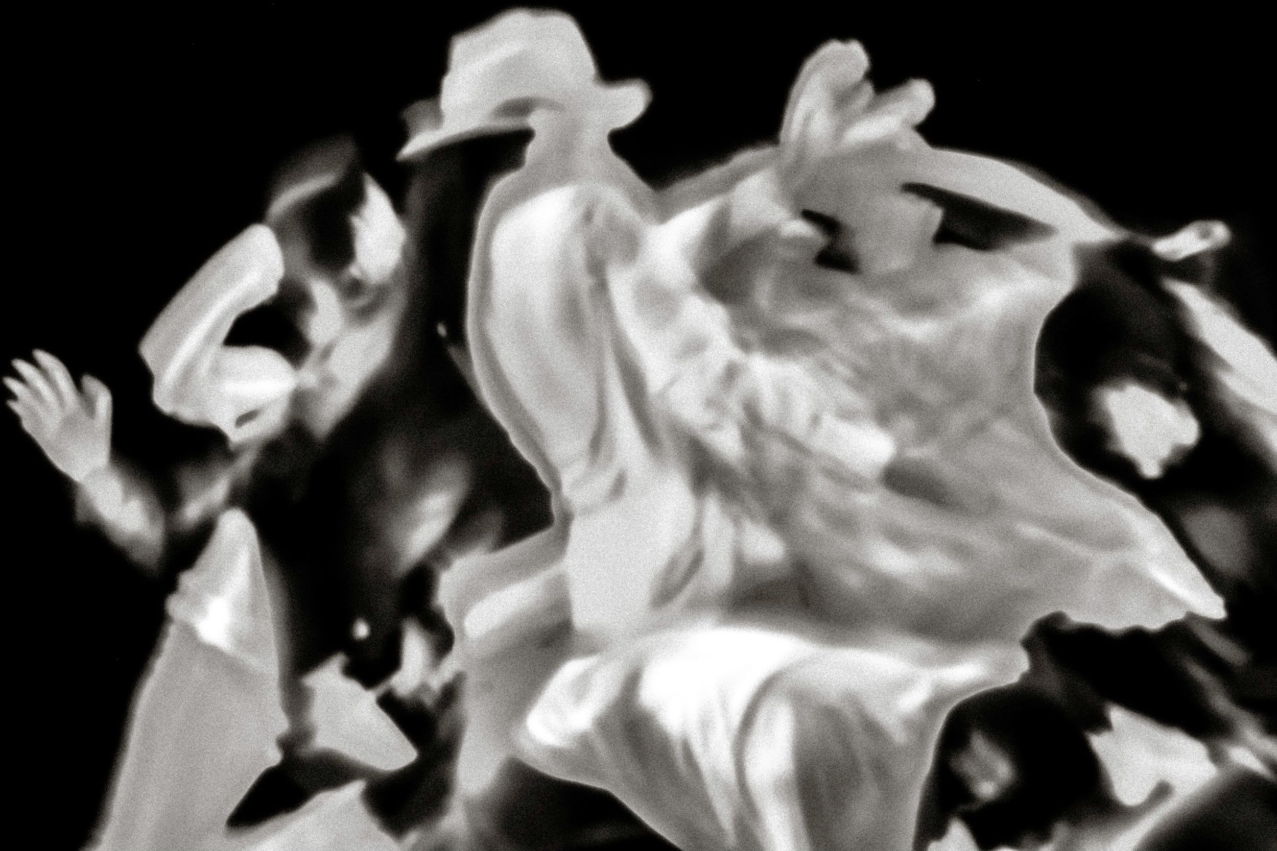 Black and white blurred motion photograph of dancers performing energetically in flowing white costumes.