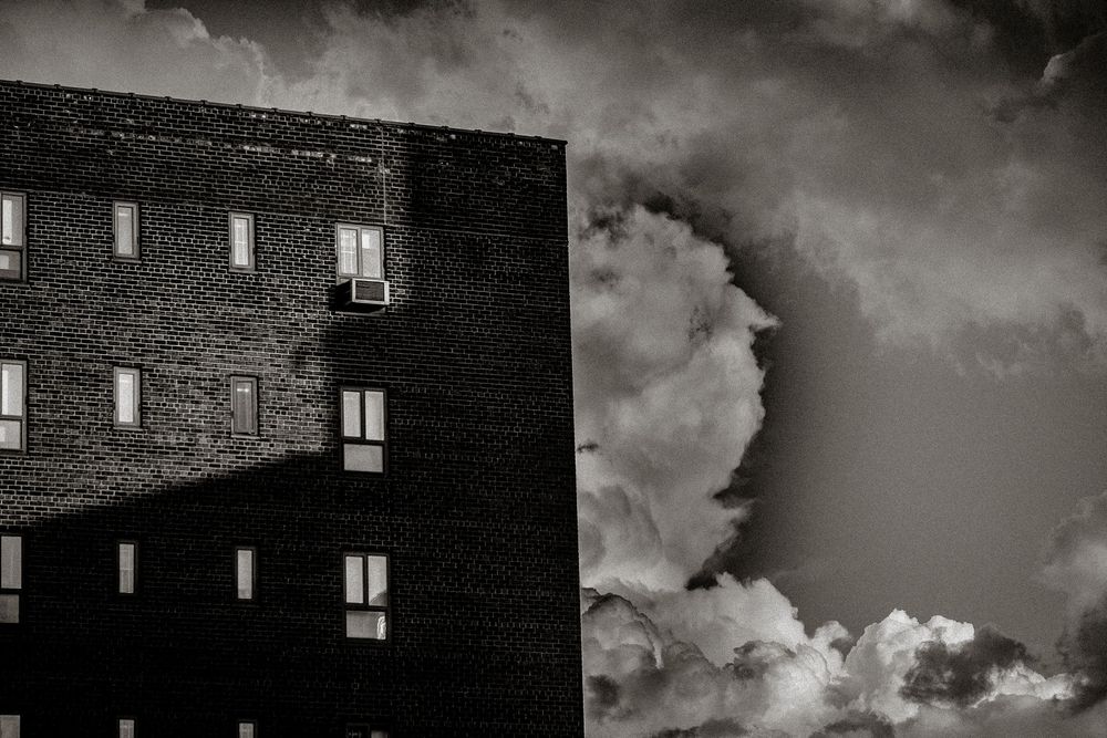 Black and white photo of a brick building beside dramatic storm clouds in the sky.