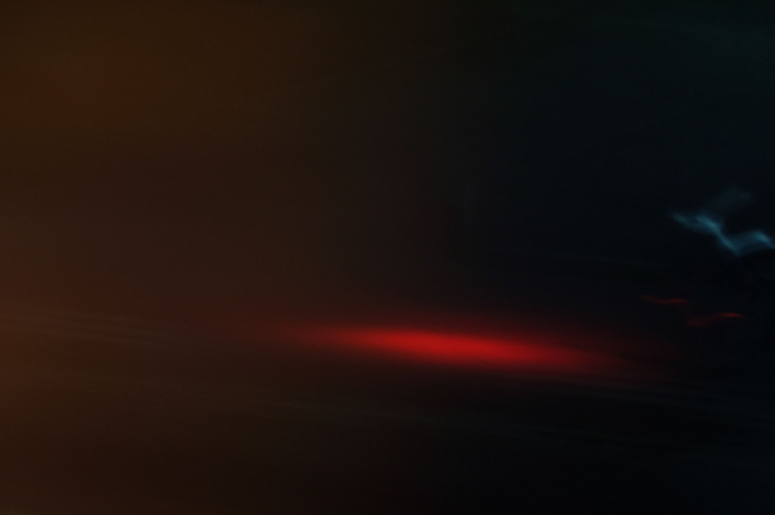 Dark stormy sky with dramatic red light streak and blue lightning bolt illuminating the night clouds.