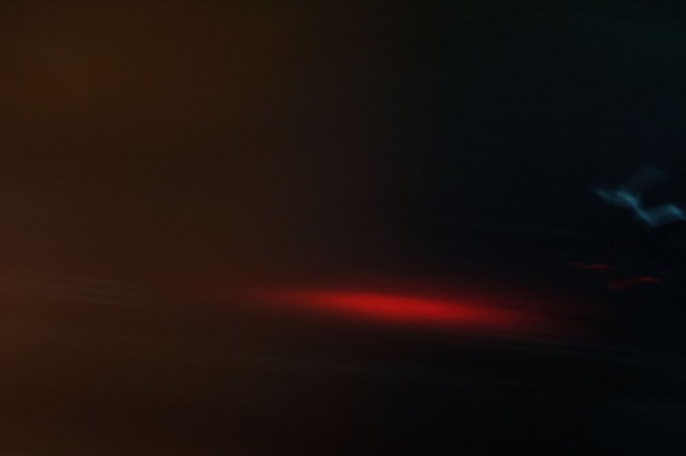 Dark stormy sky with dramatic red light streak and blue lightning bolt illuminating the night clouds.