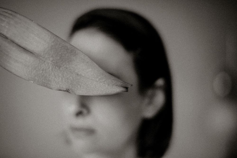 Black and white photo of a leaf in sharp focus in foreground with blurred woman in background.