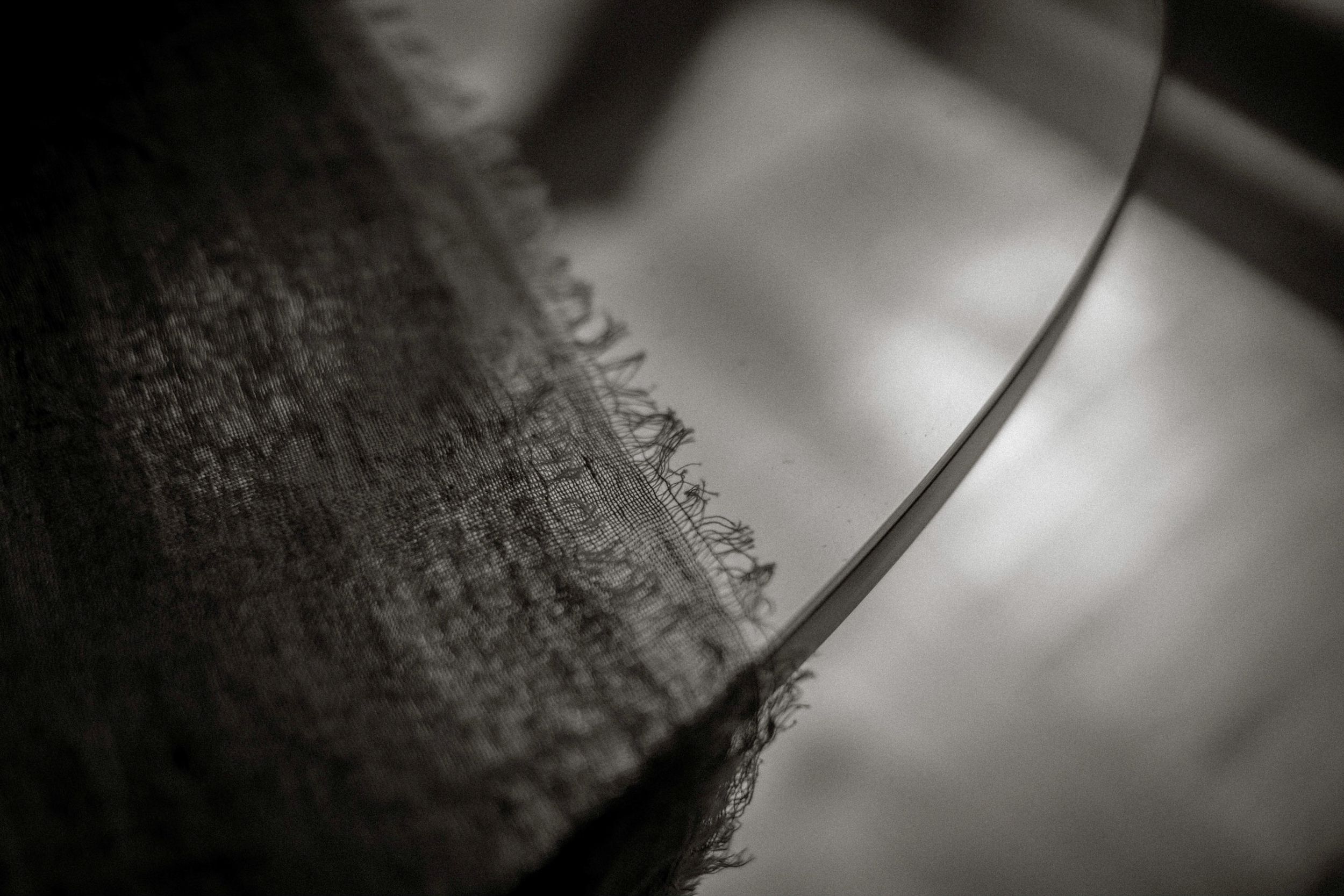 Close-up black and white macro photo of frayed fabric edge with blurred background.