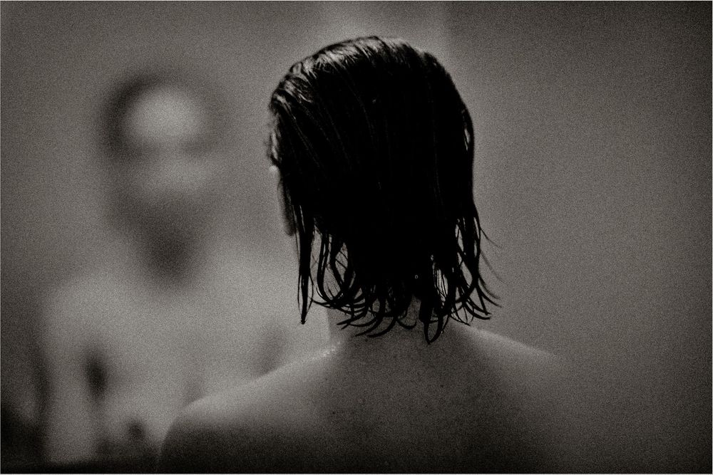 Black and white photo of a person with wet dark hair viewed from behind, reflected in a mirror.
