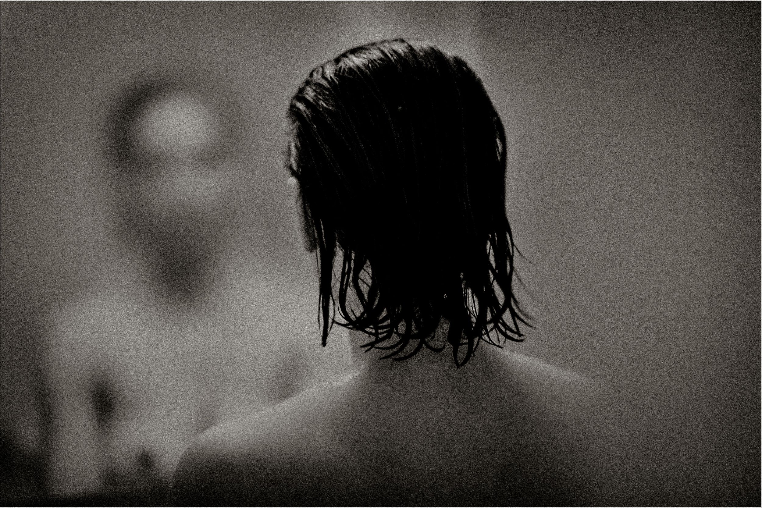 Black and white photo of a person with wet dark hair viewed from behind, reflected in a mirror.