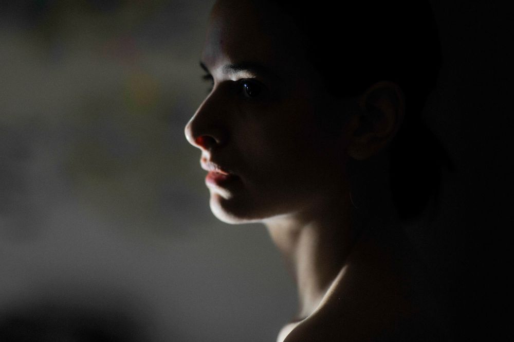 Profile of a young woman in dramatic side lighting against a dark background, showcasing elegant facial features.