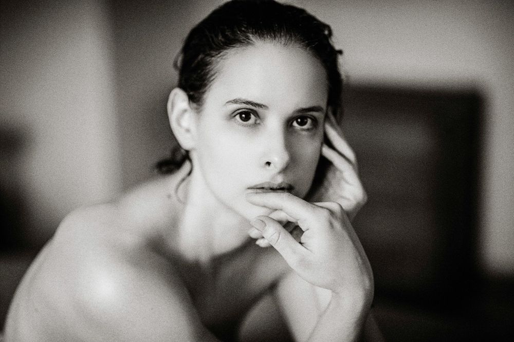 Black and white portrait of a young woman with dark hair resting her chin on her hand, gazing thoughtfully.
