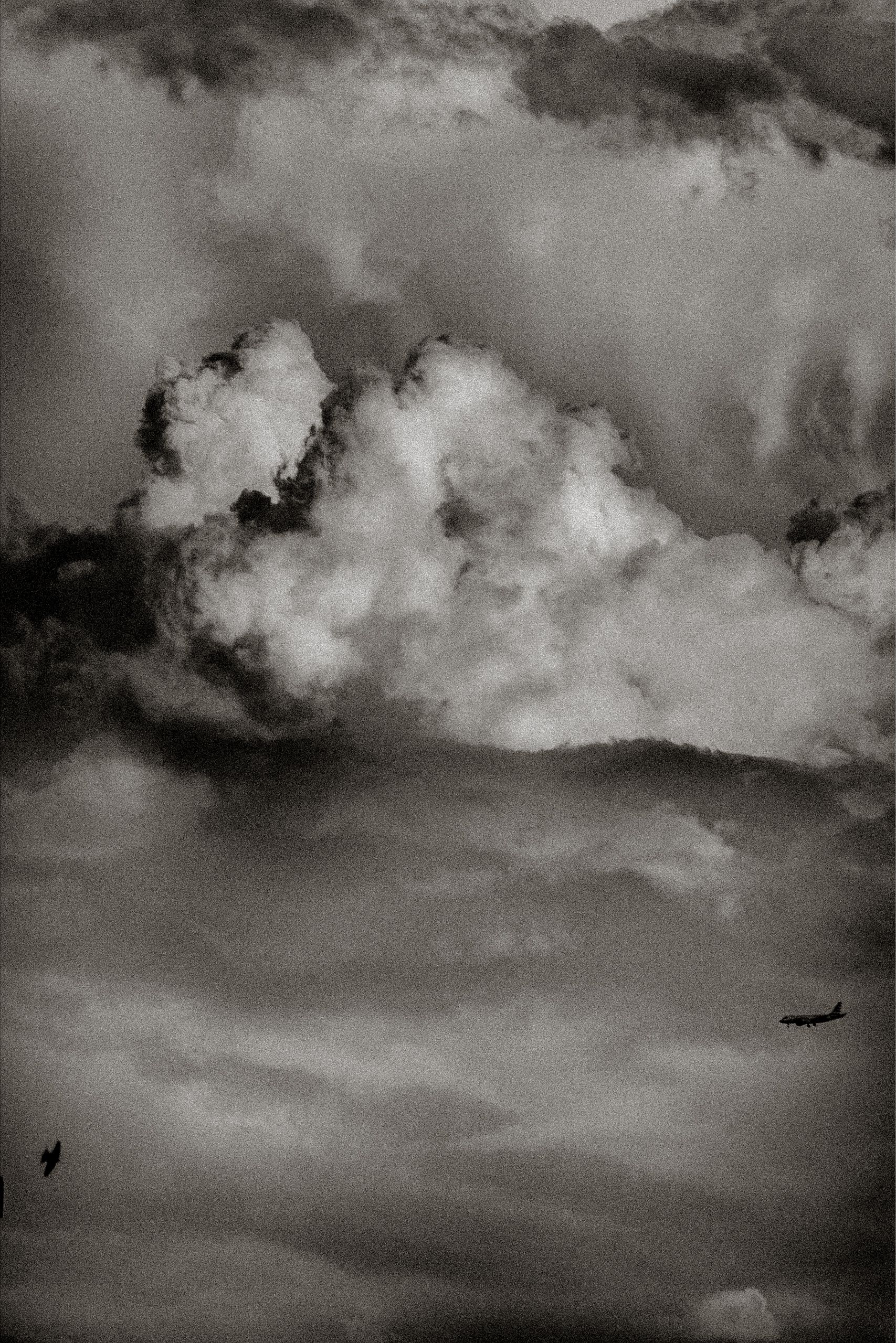 Black and white dramatic cloudscape with billowing cumulus clouds and two small aircraft silhouetted against stormy sky.