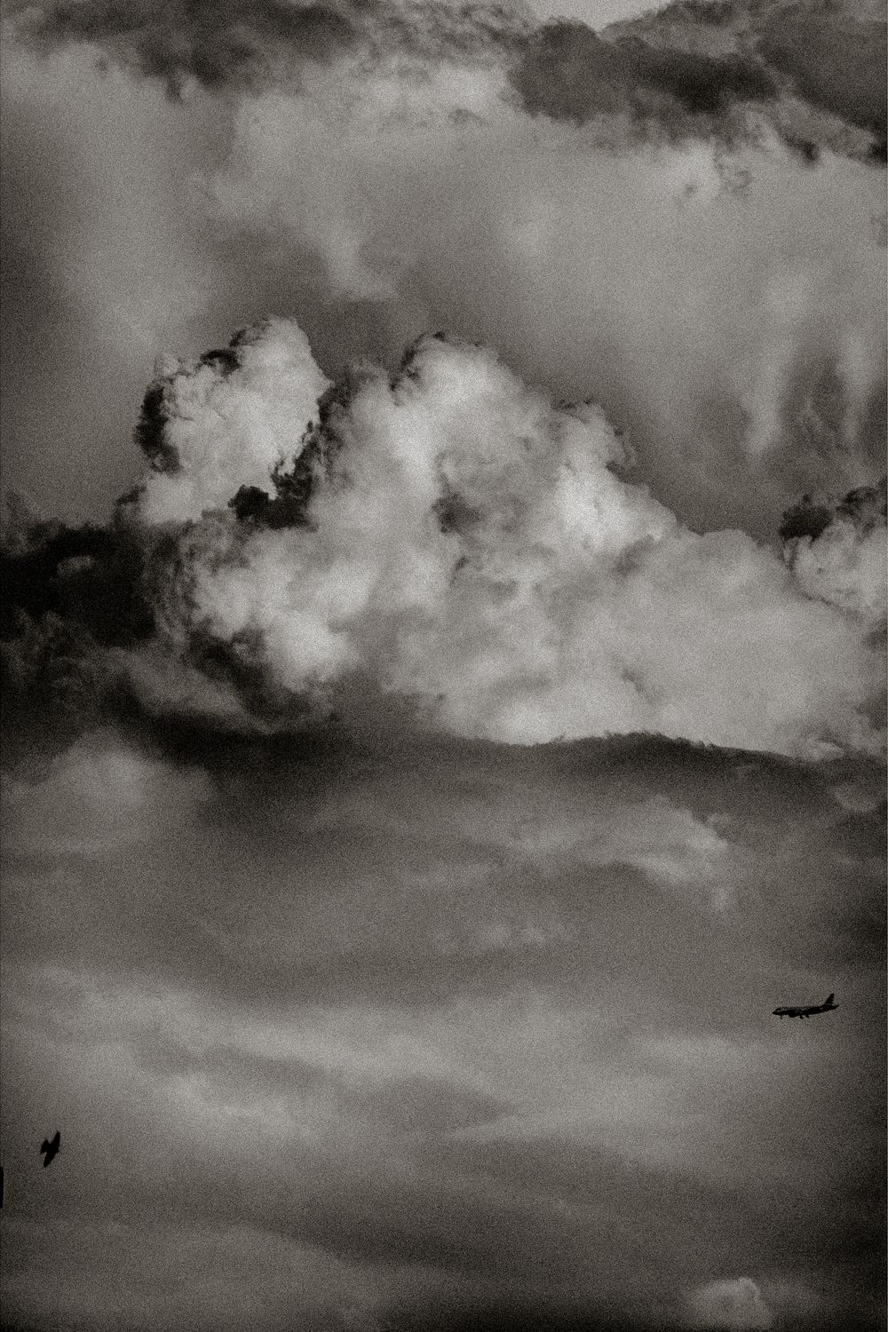Black and white dramatic cloudscape with billowing cumulus clouds and two small aircraft silhouetted against stormy sky.