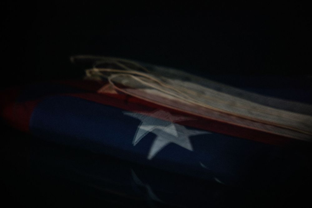 Close-up of a folded American flag with a white star visible, dramatically lit against a dark background.