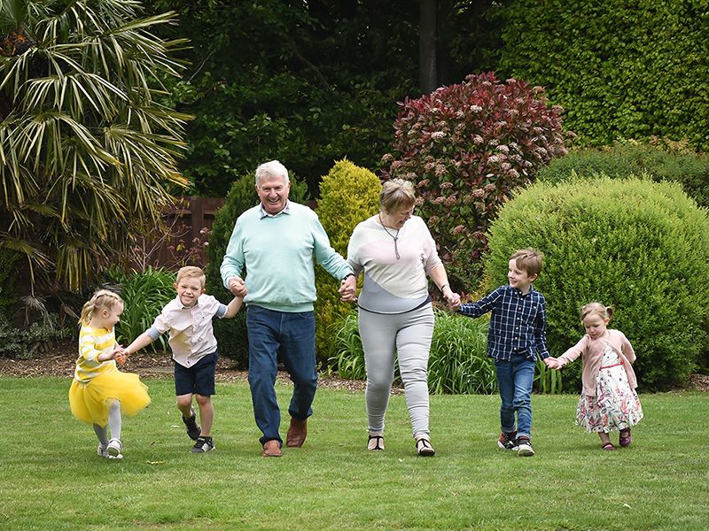 Family walking hand-in-hand in a sunny backyard with lush green plants and shrubs.