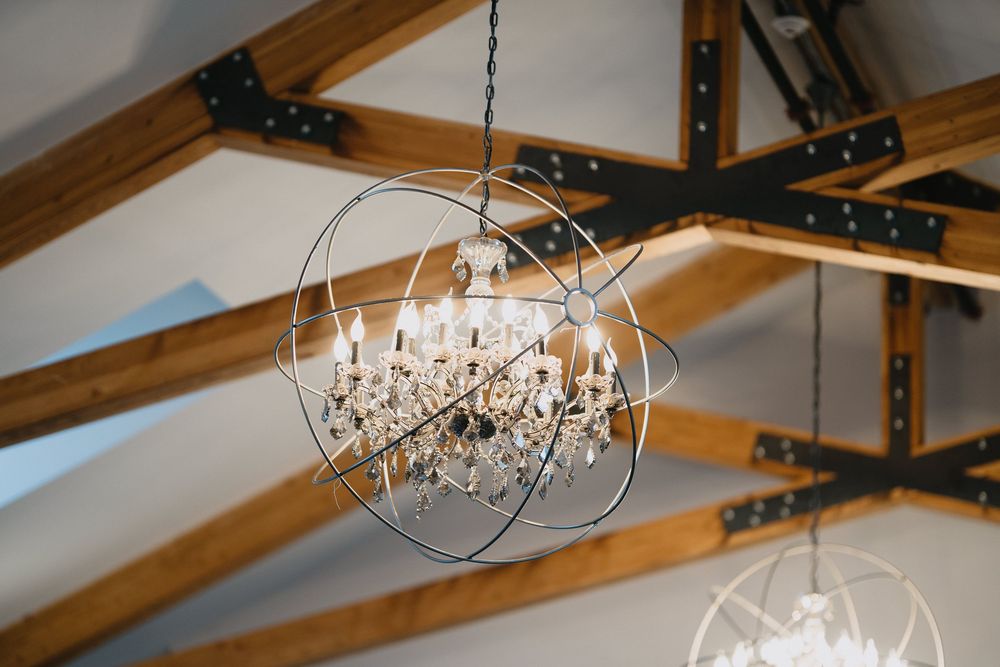 Crystal chandelier with metal orb frame hanging from rustic wooden beam ceiling in elegant venue.
