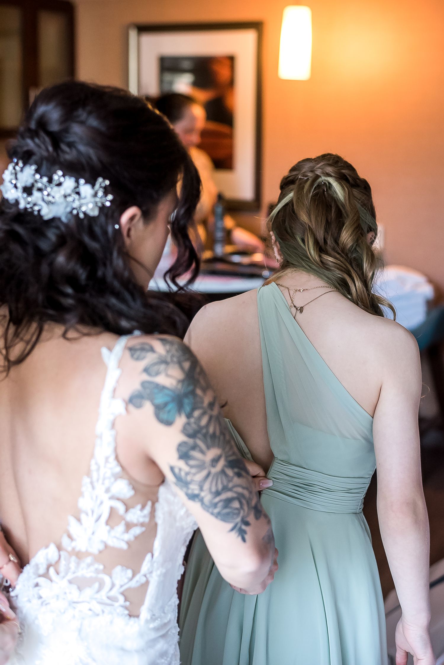A bride helps her bridesmaid while getting ready together.