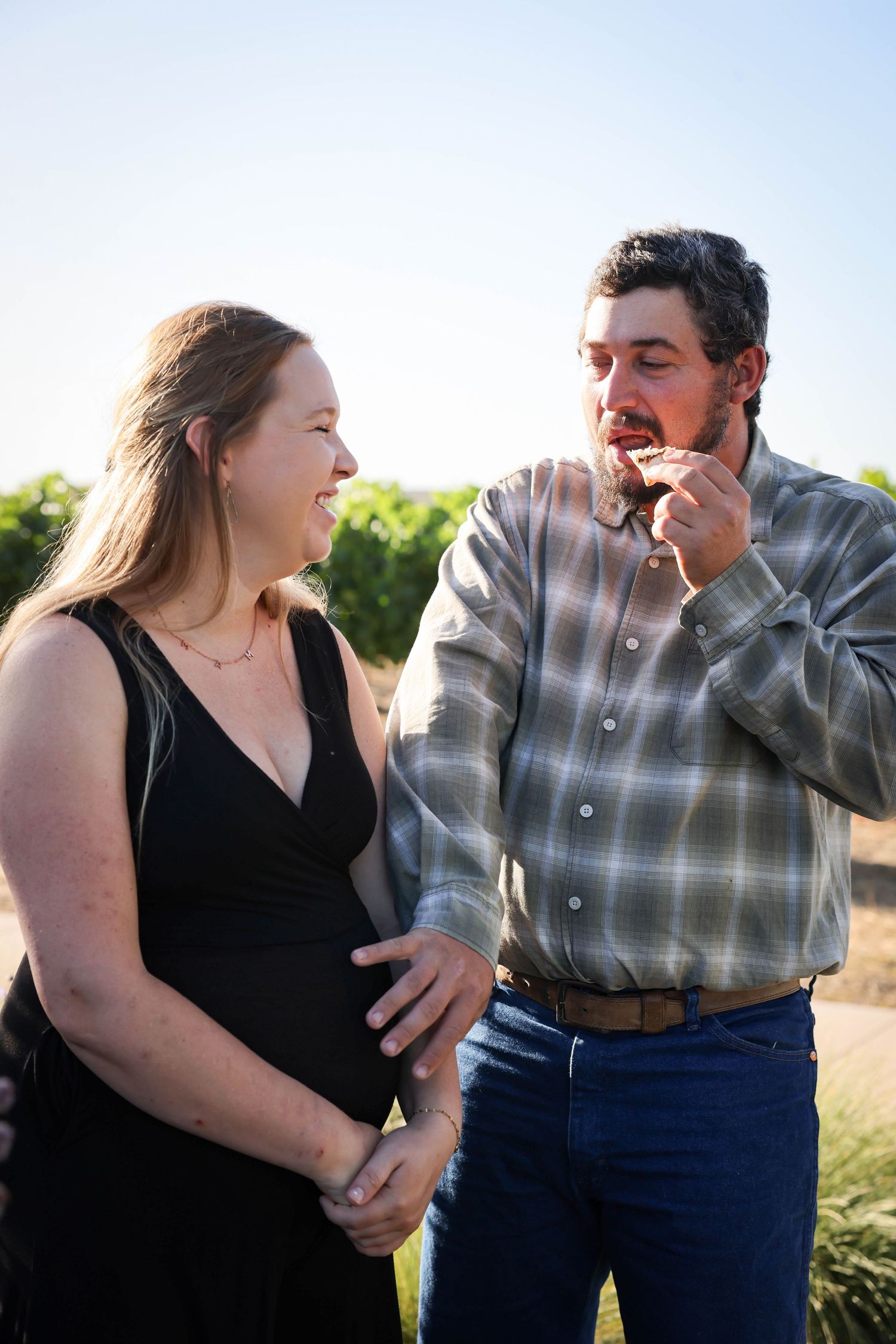Funny photo of couple, man is in the middle of eating pizza during maternity photoshoot at sunset in Paso Robles California