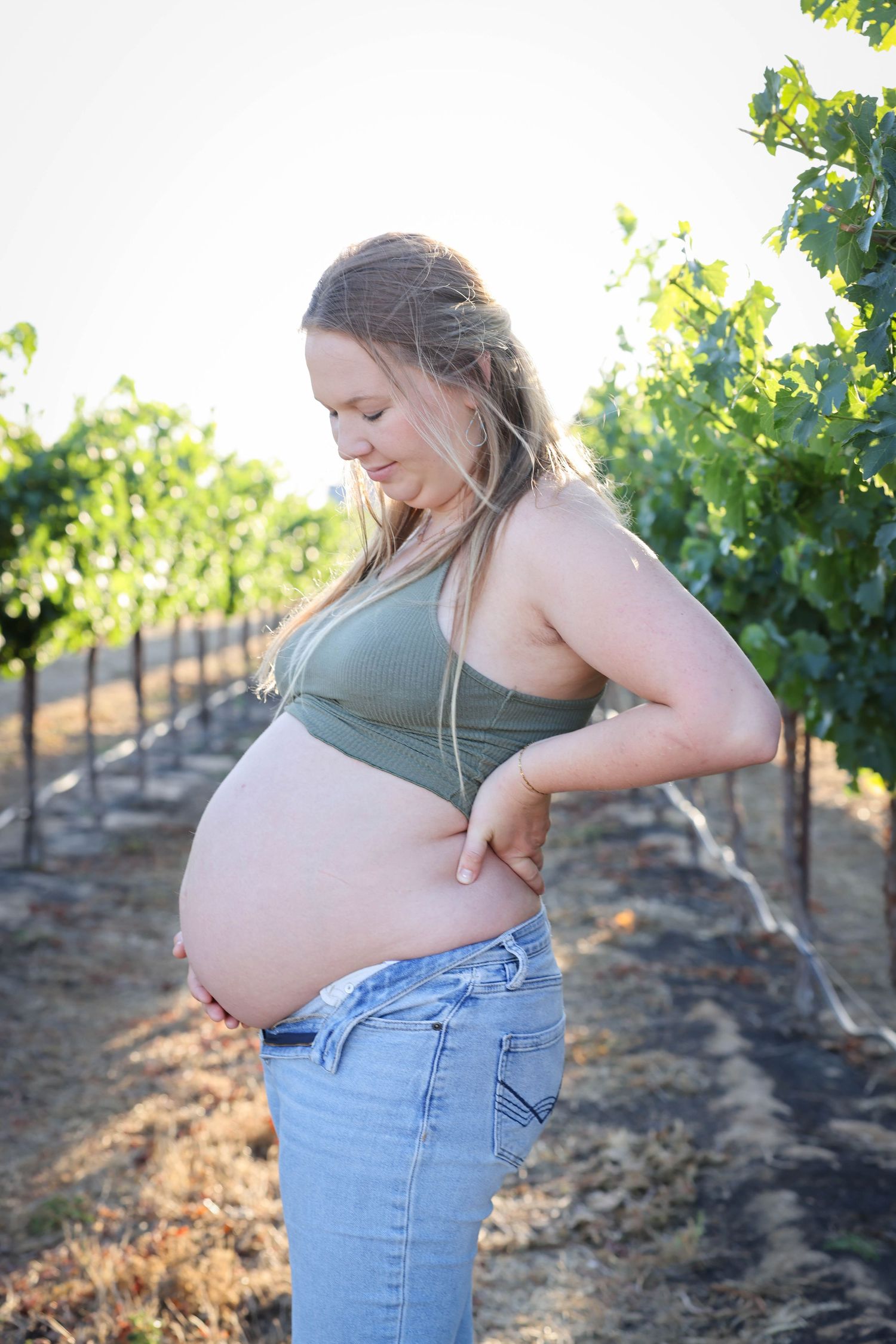 Woman embraces her growing belly during a sunset maternity portrait session in the vineyards in Paso Robles California