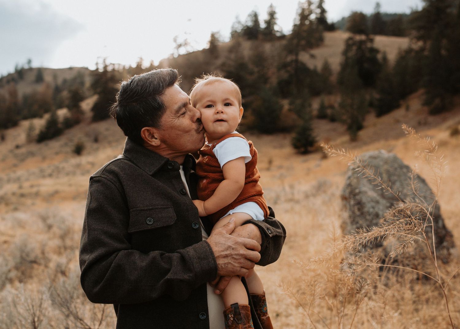 Grandfather holding and kissing his grandchild during a fall family photography session near Penticton, BC.